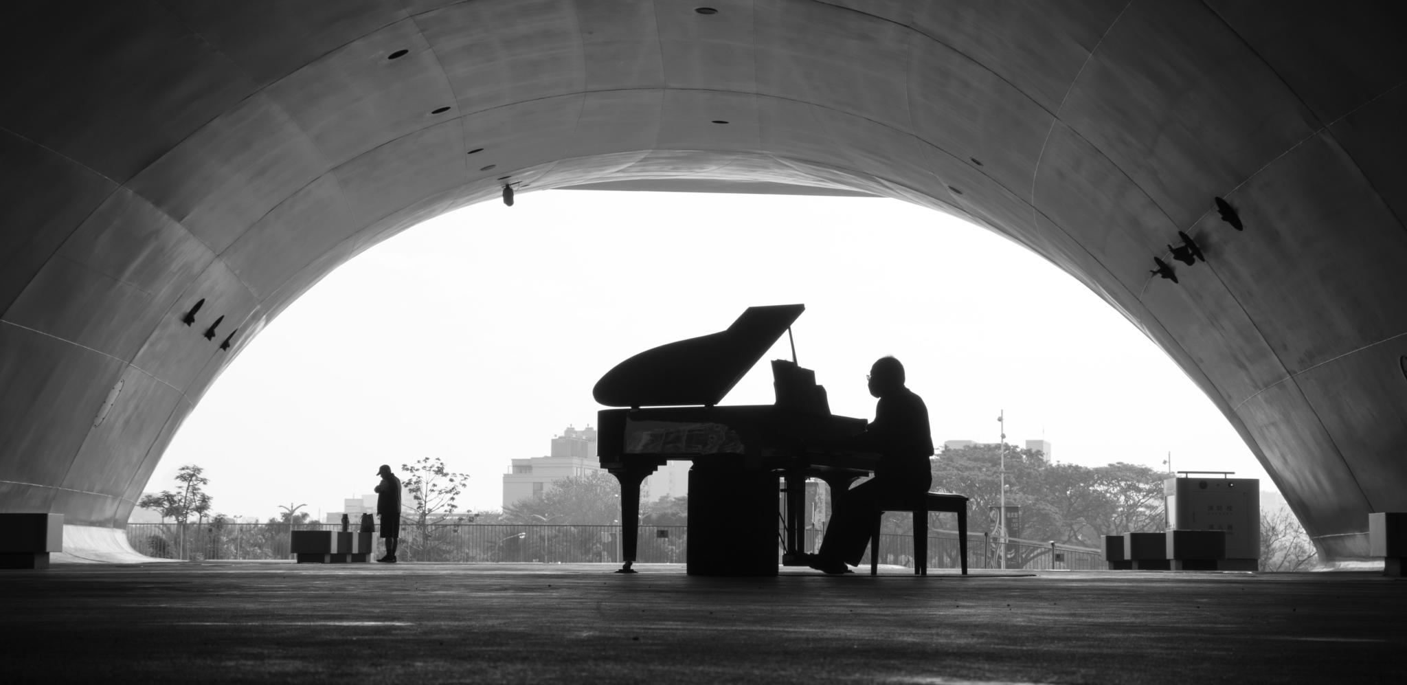 A silhouette of a person playing piano under an architectural arch.