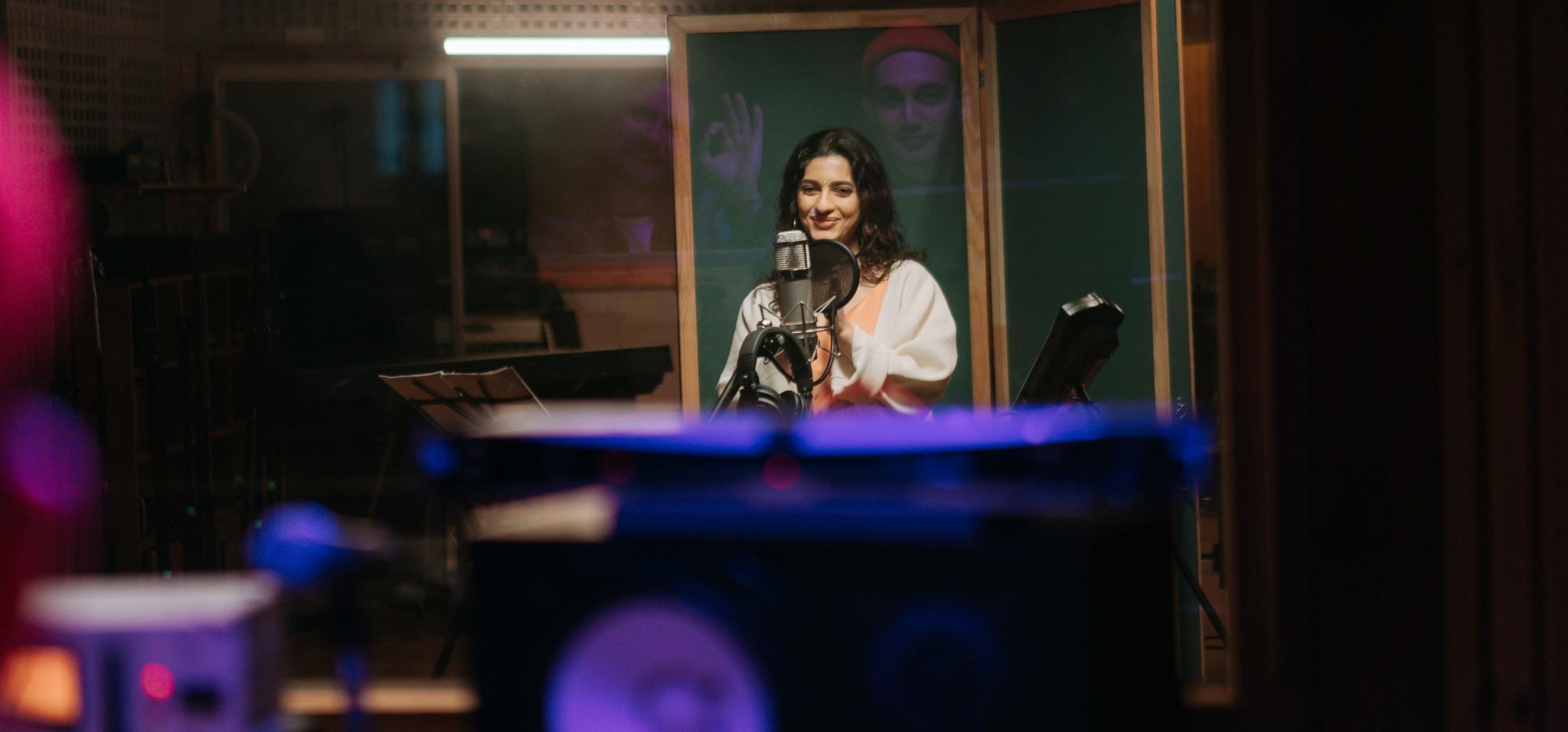 A singer in a recording studio with visible audio equipment in the foreground.