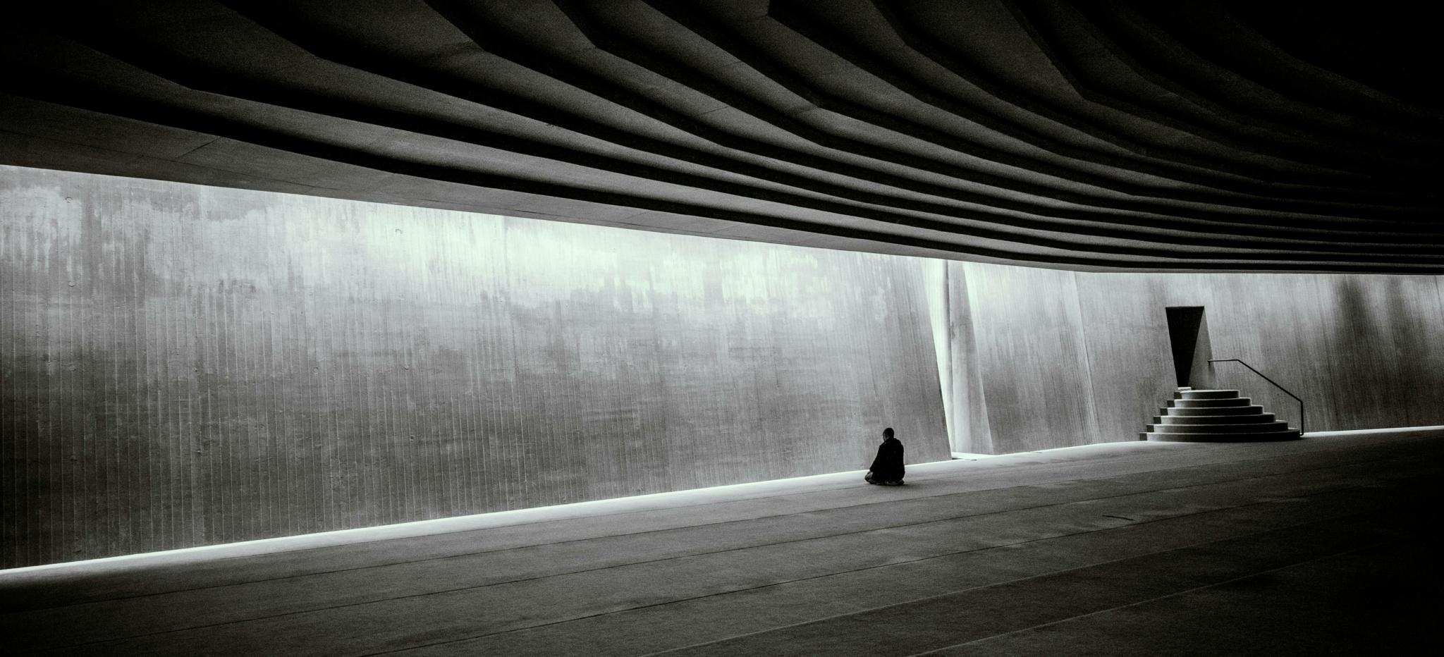 A minimalist architectural interior with a person sitting quietly.