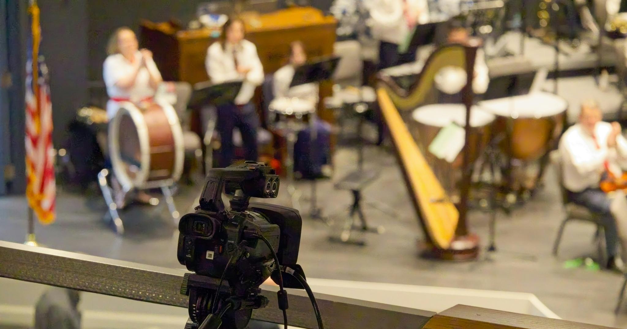 Tripod-mounted video camera filming a live orchestra performance