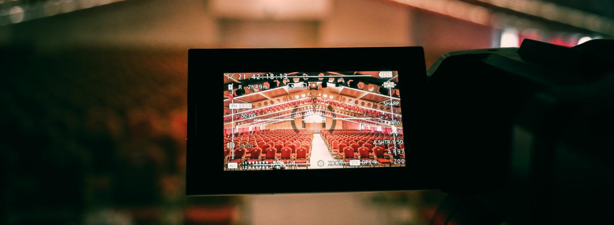 Camcorder LCD screen showing an auditorium with red seats and recording settings