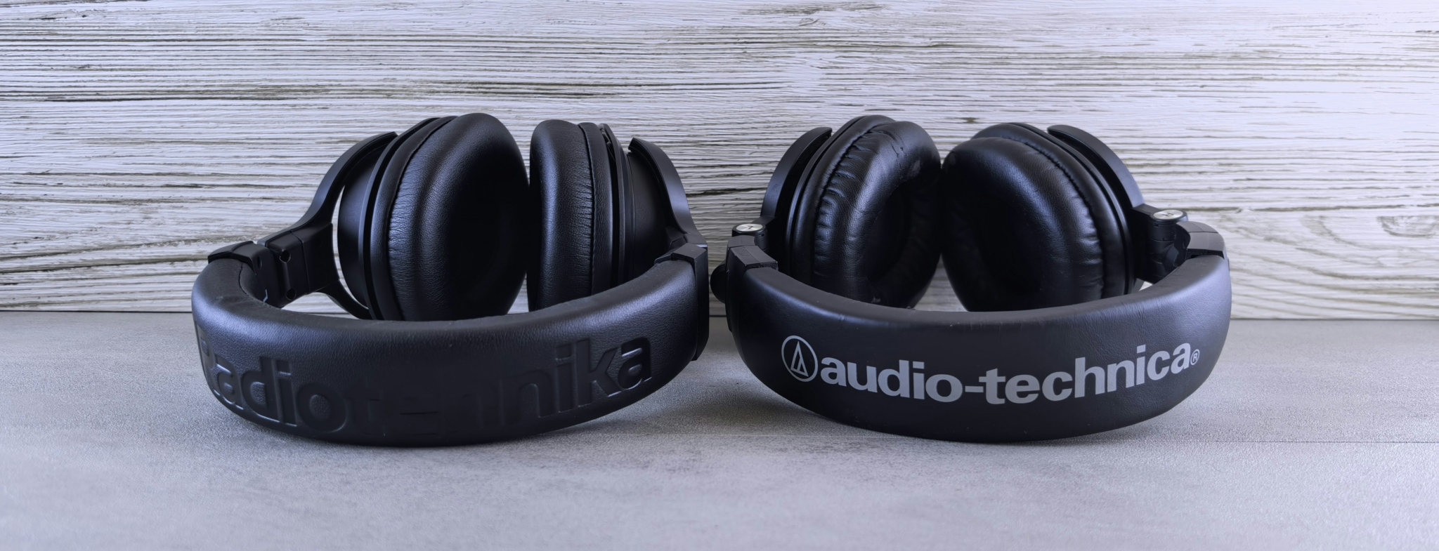 Two pairs of headphones resting on a surface, one branded Audio-Technica and the other with unreadable branding.