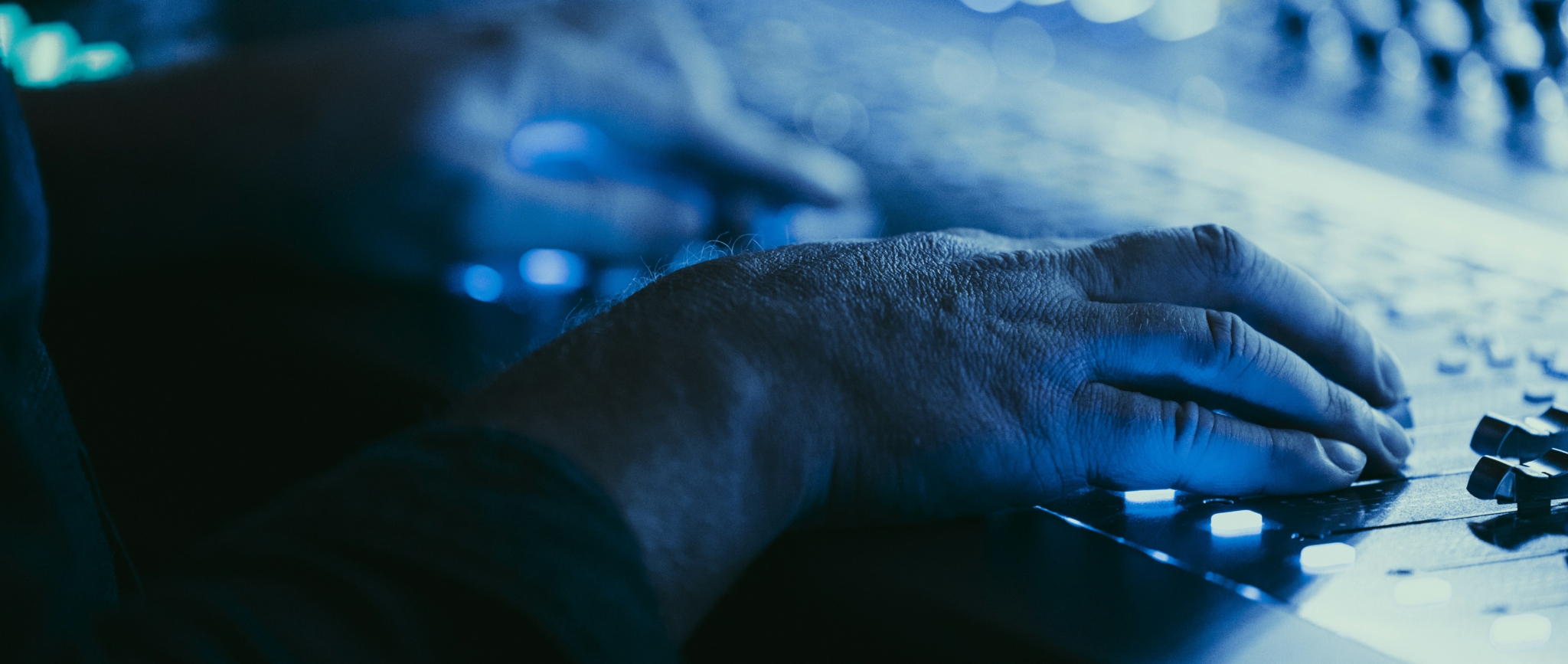 Close-up of a hand adjusting audio settings on a mixing console with blue lighting.