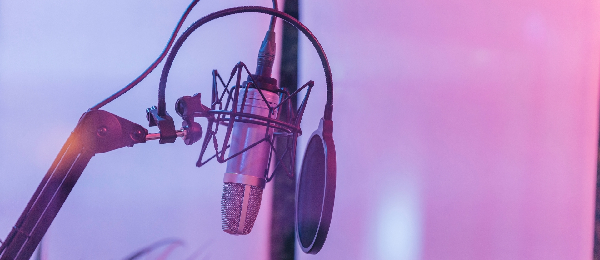 Close-up of a condenser microphone with a pop filter and adjustable boom arm in a studio setting.