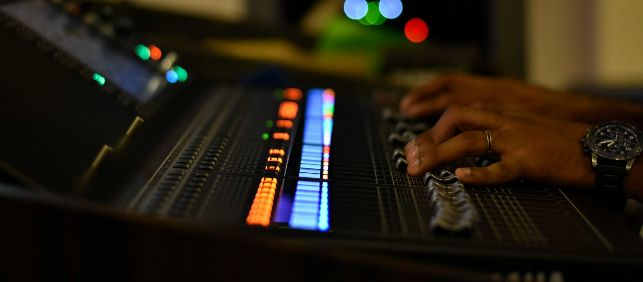 Audio mixing console with illuminated faders and hands adjusting the controls.