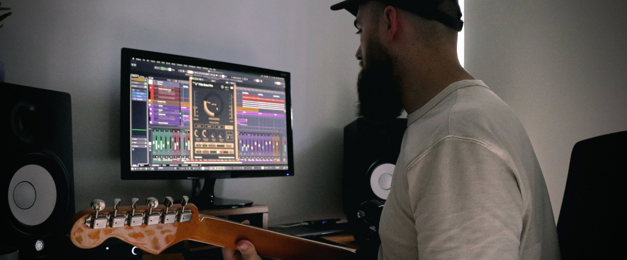Person playing guitar in front of a computer with audio software interface visible and recording settings in 32-bit to 24-bit in Logic Pro