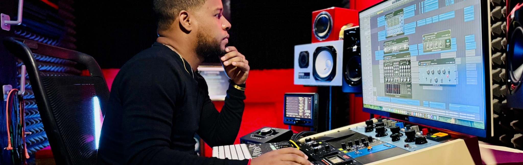 A music producer working in a professional studio with various audio equipment and software visible.