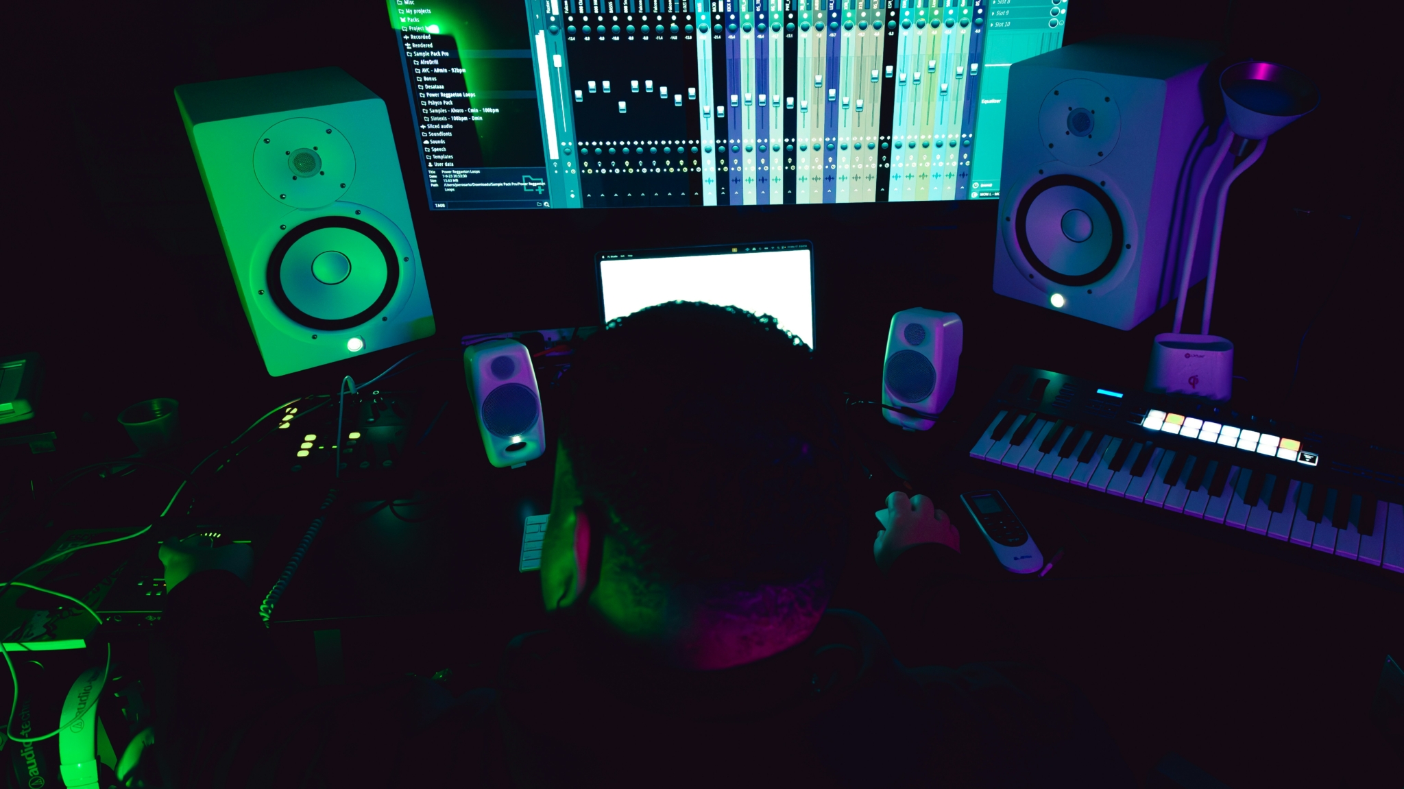 Persona trabajando en un estudio de producción musical con diferentes equipos de audio y software.