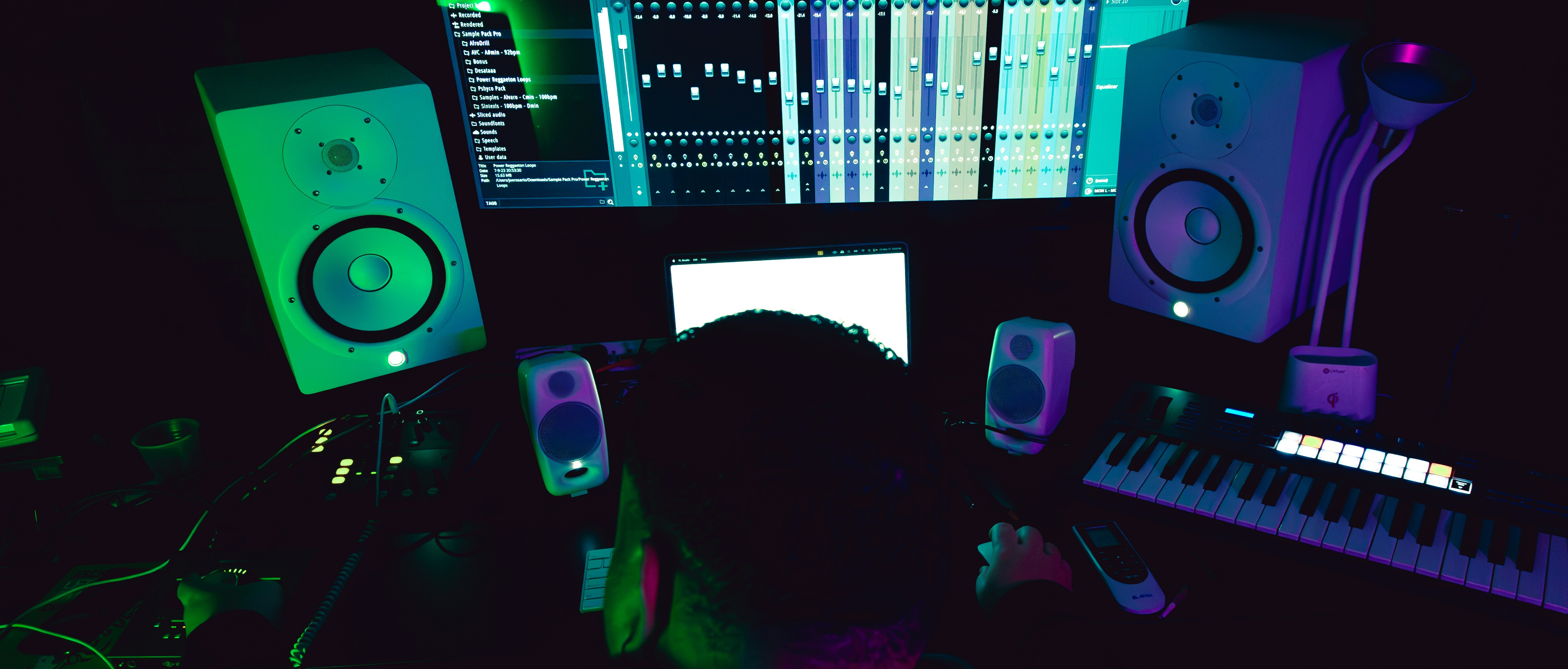 persona trabajando en un estudio de producción musical con distintos equipos de audio y software